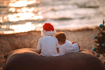 Two little boys on the beach at Christmas with a New Year tree.