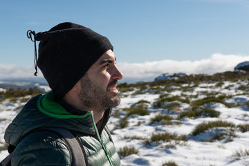 YOUNG CAUCASIAN MAN EQUIPPED WITH MOUNTAIN CLOTHES ENJOYING A TREKING WALK IN SNOWY LANDSCAPE WITH BLUE SKY AND SUNSHINE