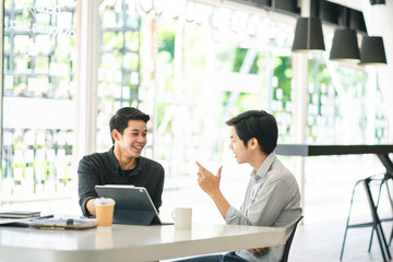 Young Asian businessmen using a digital tablet to discuss information in a modern business working space.