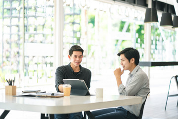 Young Asian businessmen using a digital tablet to discuss information in a modern business working space.