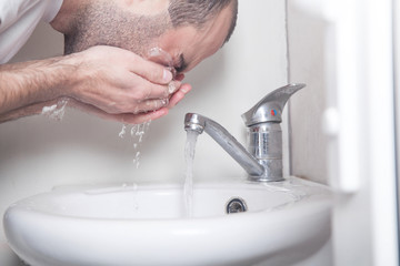 Caucasian man washing face in bathroom.