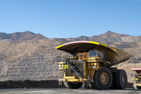 Big yellow mining truck hauling rock in dusty open-pit mine