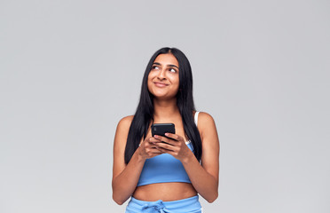 Studio Shot Of Causally Dressed Young Woman Using Mobile Phone Looking Off Camera