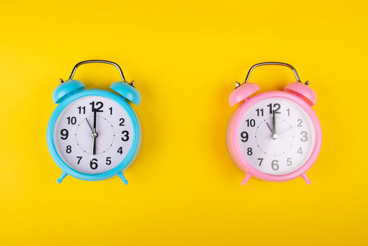 Two alarm clocks on a bright yellow background showing different time as the concept of a morning person and a night owl