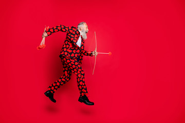 Full body photo of funky crazy aged guy cupid jumping up high hobby making feelings couple shoot love arrows wear hearts pattern suit isolated red color background