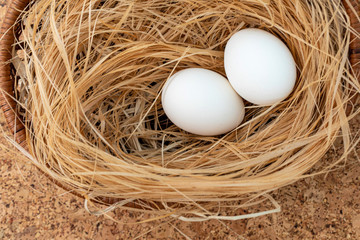 White chicken eggs are in a wicker basket with straw on cork. Easter.