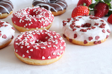 Sweet and colourful donuts glazed with sprinkles and frosting. Set of different type of doughnuts on white background. Fresh, sweet strawberries in the background, soft focus. Valentines day concept.