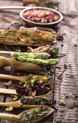 Assortment of dry tea in spoons and bowl on a wooden background.