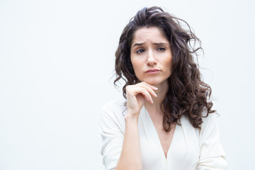 Fototapeta na wymiar Thoughtful female customer leaning chin on hand, looking away. Wavy haired young woman in casual shirt standing isolated over white background. Pensive woman or advertising concept