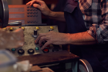 Close-up of senior manual worker standing and turning on the machine before the work in the plant