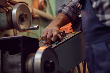 Close-up of operator in overalls controlling the work of machine using buttons in the factory