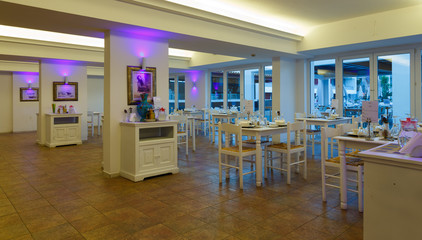 evening interior of the restaurant with white furniture and tables in resort European hotel, Greece