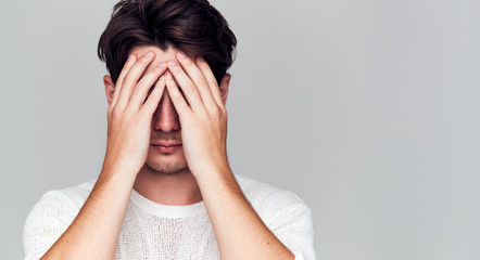 Studio Portrait Of Ashamed Young Man Covering Face With Hands