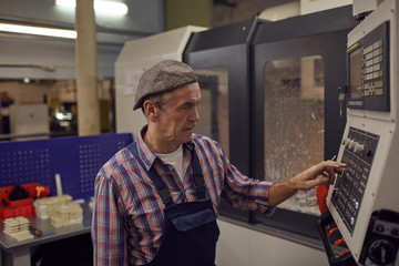 Senior operator in overalls standing in the factory and regulating the operation of the machine