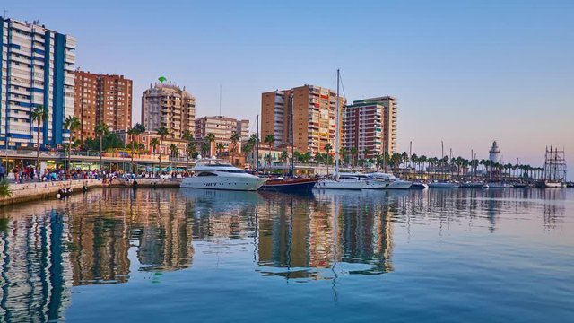 MALAGA, SPAIN - SEPTEMBER 26, 2019: The evening walk in Malaga port with a view on Muelle Uno pier with moored yachts, line of cafes and modern high rises, reflected in sea, on September 26 in Malaga