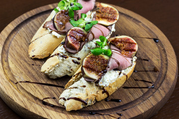 sandwich with figs and meat on a wooden plate, a snack with figs and duck	