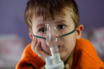 Little boy in a mask, treatments respiratory tract with a nebulizer at home. Baby sits with a...