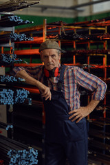 Fototapeta na wymiar Portrait of mature mechanic in coveralls standing near the metal pipes and looking at camera in warehouse