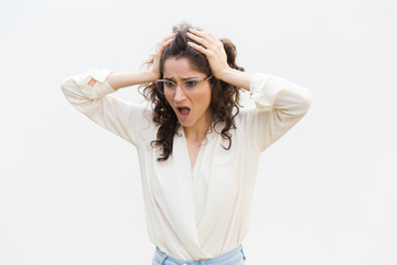 Naklejka premium Shocked upset woman in glasses gasping, holding head and staring away at copy space. Wavy haired young woman in casual shirt standing isolated over white background. Failure concept