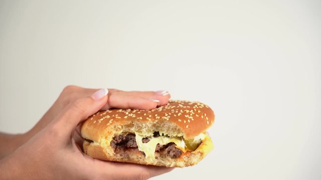 Woman eating tasty juice cheese burger. Closeup side view of bitted cheeseburger in hands of woman isolated on white background. Real time 4k video footage.