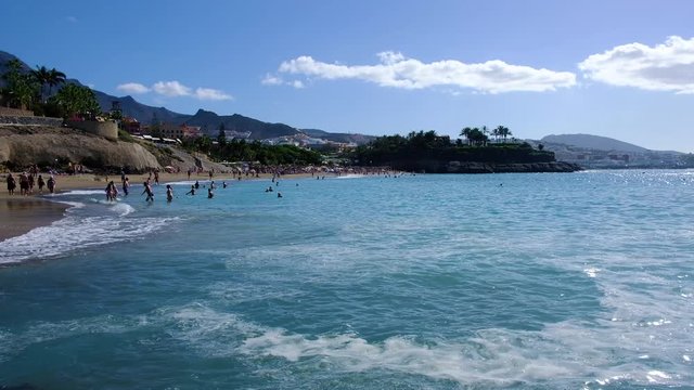 COSTA ADEJE, TENERIFE, SPAIN - NOVEMBER 2019: People lay on the sand and swim in the ocean at tropical beach.