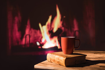 book and cup of hot drink on the wood table near Christmas fireplace. Cozy atmosphere. Still life. Winter and Christmas holidays concept