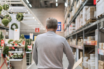 Tall gray-haired man shopper walking with trolley in a large hardware store before christmas. Back...