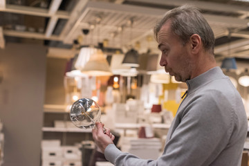 Astonished middle aged man with fear and excited face looking on huge incandescent edison lamp with...