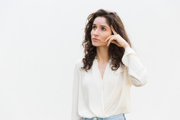 Pensive woman touching head and looking up at copy space. Wavy haired young woman in casual shirt...