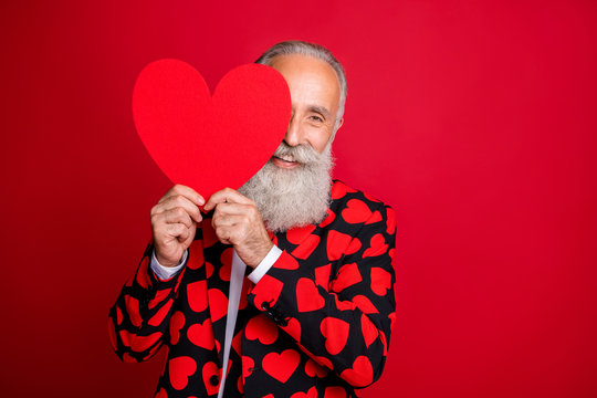 Photo of funky mature man cupid amour hold paper heart shape postcard hide half face flirty coquettish mood wear hearts pattern suit blazer shirt tie isolated vibrant color background