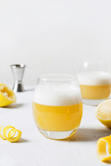 Whiskey sour cocktail - bourbon with lemon juice, sugar syrup and egg white in glass on wooden board on white. Vertical orientation.