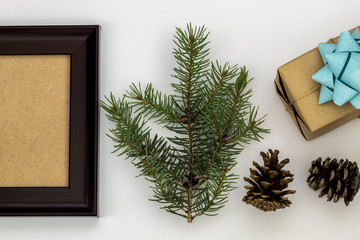 Composition Using Pine Branch, Empty Picture Frame, Gift Box, and Two Pine Cones on White Background