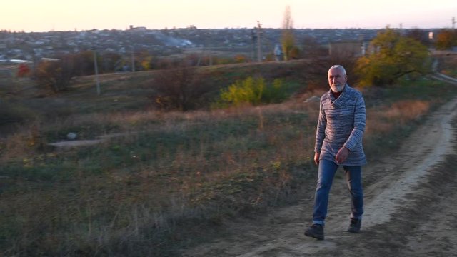  Eldery man with gray hair and beard walking in the countryside at sunset rustic style