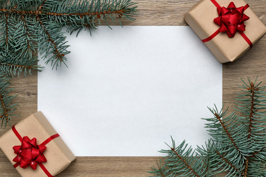 Christmas or New Year composition. White sheet of paper with copy space, gift boxes and Christmas tree branches on wooden background. Flat lay, top view, horizontal layout