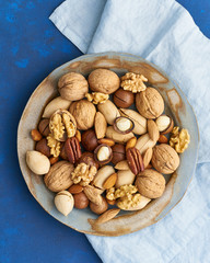 Classic blue in food. Mix of nuts on plate - walnut, almonds, pecans, macadamia and knife for opening shell. Healthy vegan food. Clean eating, balanced diet. Top view