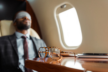 selective focus of glasses on table near african american businessman in plane