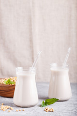 Organic non dairy soy milk in glass and wooden plate with soybeans on a gray concrete background.