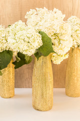 Golden glittered bottles with hydrangea flowers. White flowers in gold vases
