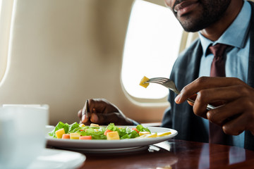 cropped view of african american man eating salad in private plane