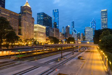 Fototapeta na wymiar Evening twilight exterior skyline shot of downtown Chicago at night with building cityscape illuminating the dark sky view over train track rail yard for loop transit system