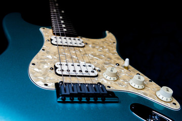 A detail of a Light Blue electric guitar on a black background.