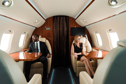 selective focus of handsome african american businessman and attractive businesswoman sitting in private plane