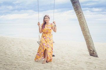 Beautiful woman in yellow dress smiling on a swing under a coconut palm.