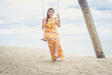 Beautiful woman in yellow dress smiling on a swing under a coconut palm.