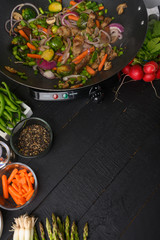 Roasting meat with vegetables, on a black wooden background. Culinary, gastronomy. Vertical frame. Tasty and healthy food.