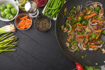 Asian cuisine, Flat lay, cooking and frying meat with vegetables. On a black wooden background with space, culinary background.