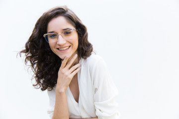 Fototapeta premium Positive stylish female student touching chin, looking at camera, smiling. Wavy haired young woman in casual shirt standing isolated over white background. Female portrait concept
