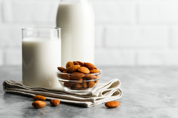 Glass reusable bottle and mug with almond milk and almonds on a marble countertop, kitchen with a...