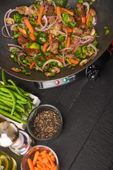 Roasting meat with vegetables, on a black wooden background. Culinary, gastronomy. Vertical frame. Tasty and healthy food.