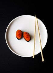 Minimalistic  flat lay with sushi or sashimi with red tobiko caviar on the white plate with Chinese chopsticks and black background